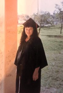 A woman wearing a black graduation cap and gown stands outdoors. She is visibly pregnant. The photo quality is old and faded.